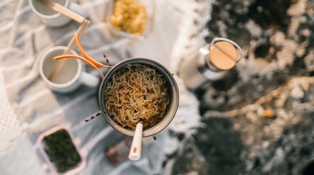クッカーでインスタントラーメンを作り白いカップを並べた山ごはんの様子