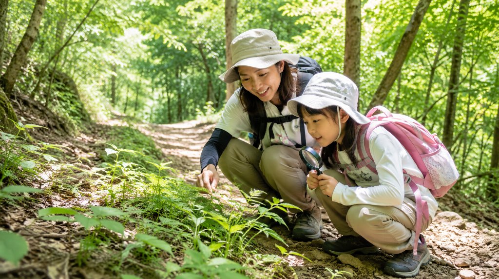 山道でしゃがんで植物を観察する親子
