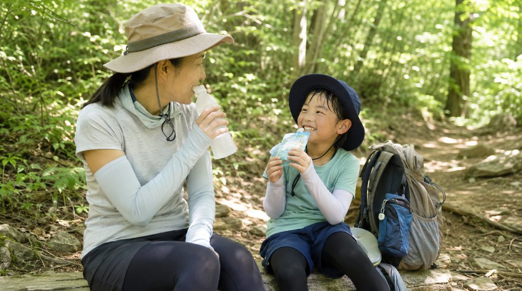 夏の登山道で休憩し水分と栄養を補給する親子