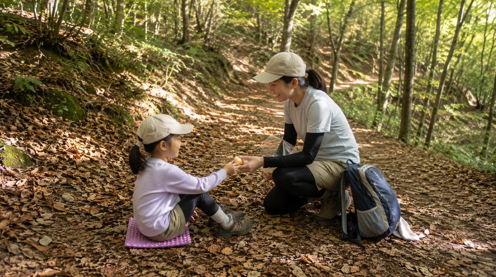 落ち葉の上の座布団に座る子どもとおやつを渡す親