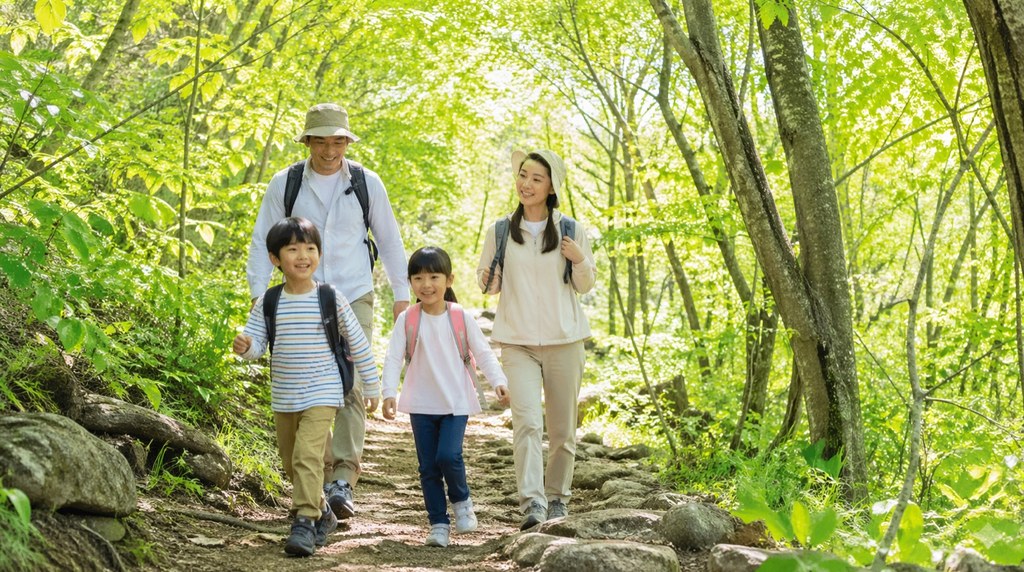 新緑の登山道を歩く子連れ登山の家族(父・母・小学生の子ども2人)