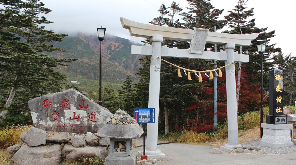 紅葉した木々の前に立つ田の原の御嶽神社の鳥居と、御嶽山登山道と刻まれた石